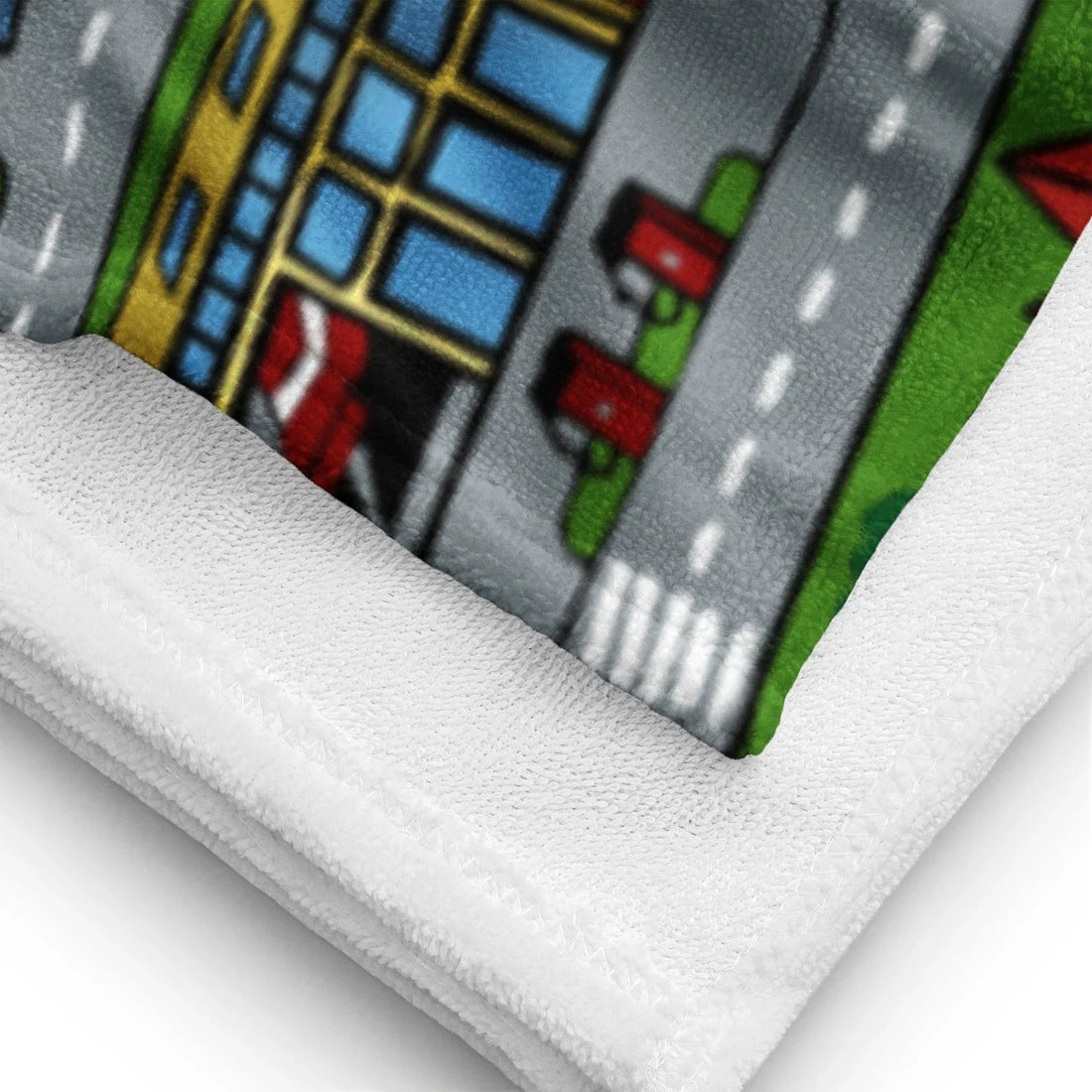 This beach towel showcases a nostalgic bird's-eye view of a miniature town playmat, complete with winding grey roads marked by white dashed lines curving around vibrant green parks. Contact us with accessibility feedback, we'd love to help!